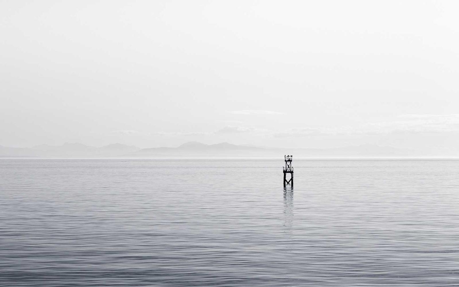 A single marker post standing in calm, misty water
